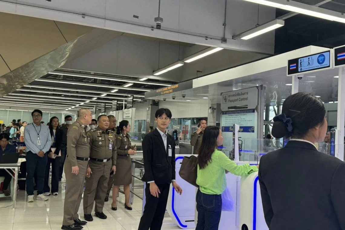 Thai immigration officers and airport staff beside the automatic e-passport channel at Suvarnabhumi Airport passport control, with a traveller using a gate